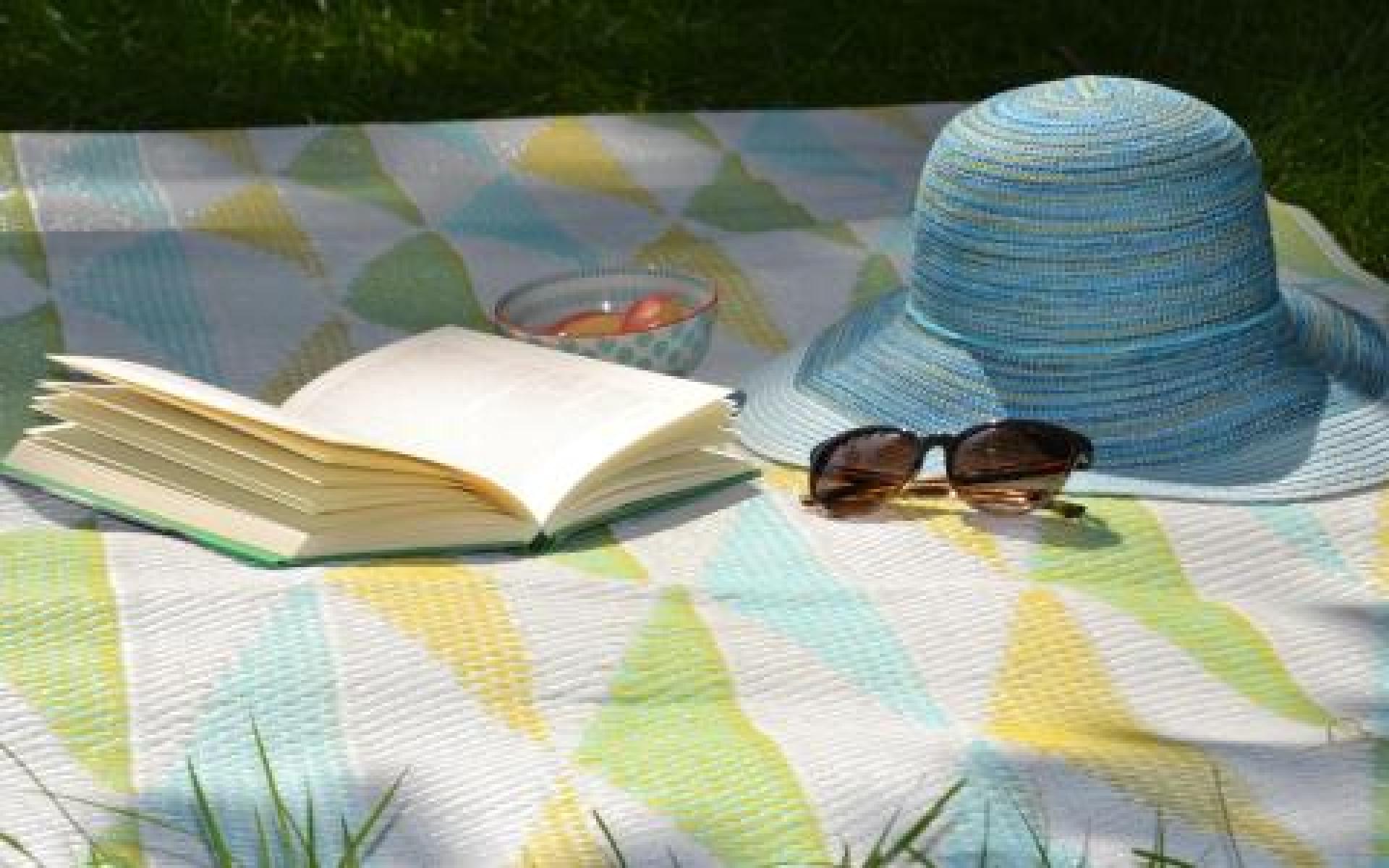 Sommerbild: Picknickdecke mit aufgeschlagenem Buch und Sonnenbrille und Sommerhut